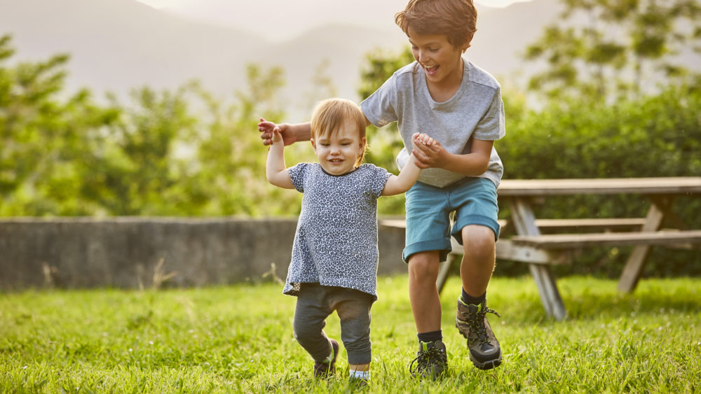 Peligro extraño | Niño feliz jugando con un niño pequeño en un campo de hierba. Los niños visten casuales. Están disfrutando en el patio trasero.