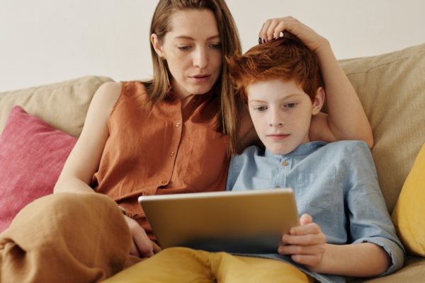 Mamá e hijo sentados uno al lado del otro mirando un dispositivo de computadora hablando.