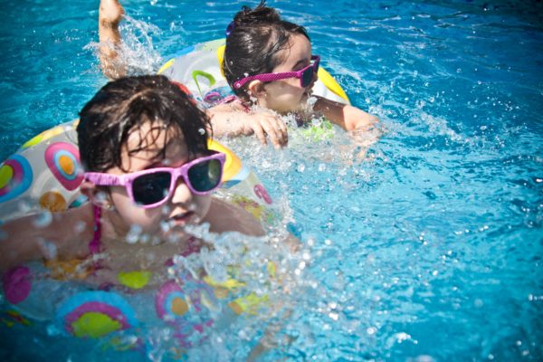 2 young girls swimming. Both are in floating rings and wearing sunglasses.