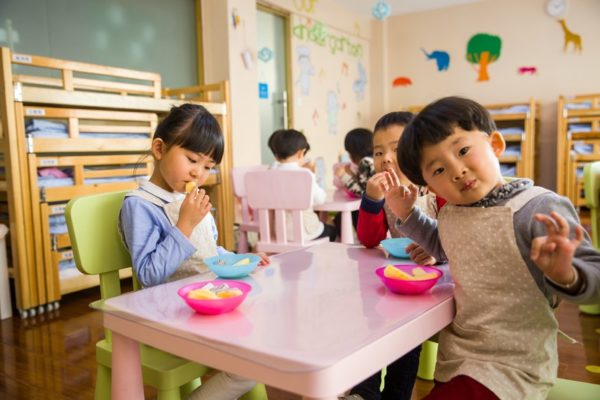3 preschoolers sitting at a classroom table having a snack.